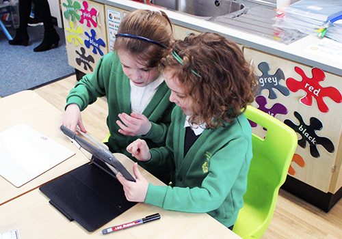 Two young girls in uniform using iPad to learn