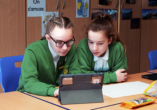 Two school girls in uniform using the iPad to collaborate
